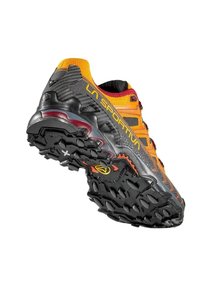 Zapatilla de trail running con parte superior negra con acentos naranjas, material texturizado y patrón distintivo de la suela para tracción.
