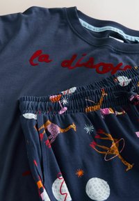 Navy cotton sweatshirt with "la disco" embroidered in red, paired with navy pajama shorts featuring colorful animal patterns and elastic waistband.