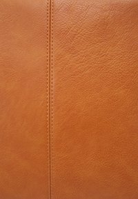Skórzany materiał w kolorze koniakowym o fakturowanej powierzchni, z centralnym szwem i subtelnym przeszyciem, ukazujący bogaty, ciepły kolor.