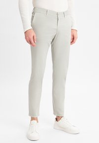 Helle graue Chinos mit schmaler Passform und glatter Textur, ausgestattet mit Fronttaschen und einem einzigen Knopfverschluss, kombiniert mit weißen Sneakern.