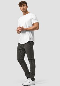Camiseta blanca de manga corta con dobladillo redondeado, combinada con pantalones ajustados grises y zapatillas blancas. Diseño simple y colores clásicos.