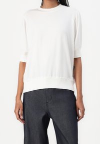 Lätt, krämfärgad skjorta med rund halsringning, trekvartslånga ärmar och rynkad nederkant, matchad med mörka denimbyxor.