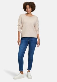 Hellbeige gestrickter Pullover mit weiten Ärmeln, kombiniert mit dunkelblauen Skinny Jeans und weißen Sneakers, mit lässigem Schnitt und strukturiertem Stoff.