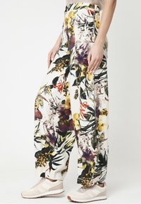 Wijd uitlopende broek met een meerkleurig bloemenpatroon, hoge taille, zijzakken, gedragen met beige en witte sneakers op een lichte achtergrond.