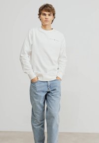 Hvid bomulds sweatshirt med ribbede manchetter, med et logo "GANT 1949" på brystet; parret med lyseblå denim jeans.