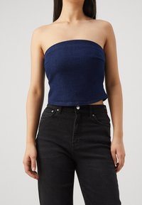 Mörkblå strapless crop top i denim, med en figurnära design och en slät textur samt rena, enkla linjer. Matchas med svarta jeans.
