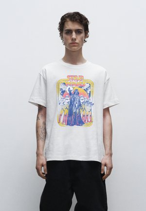 Weißes Baumwoll-T-Shirt mit einem retro Star Wars-Motiv, das Darth Vader und Sturmtruppen zeigt, umrandet mit gelben und roten Akzenten.