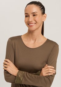 Brun långärmad topp med rundad halslinning och intrikata mönstrade detaljer vid ärmsluten, tillverkad av ett mjukt, slätt tyg.