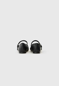 Ballerine in pelle nera con cinturini alla caviglia regolabili e design minimalista. Punta arrotondata e suola piatta.