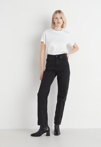 Zwarte high-waisted jeans met een rechte pijp, gecombineerd met een plain witte t-shirt met korte mouwen, gedragen met zwarte hoge enkellaarsjes.