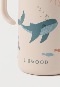 Ανοιχτό ροζ κύπελλο φτιαγμένο από σιλικόνη, με παιχνιδιάρικες σχεδόν φάλαινα και ψαριών σε μπλε και πορτοκαλί, και με χερούλι στ�ο πλάι. Μάρκα LIEWOOD στο κάτω μέρος.