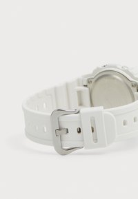 Bracelet de montre en caoutchouc blanc avec une boucle en métal argenté, doté d'un design texturé et de trous de ventilation le long du bracelet.