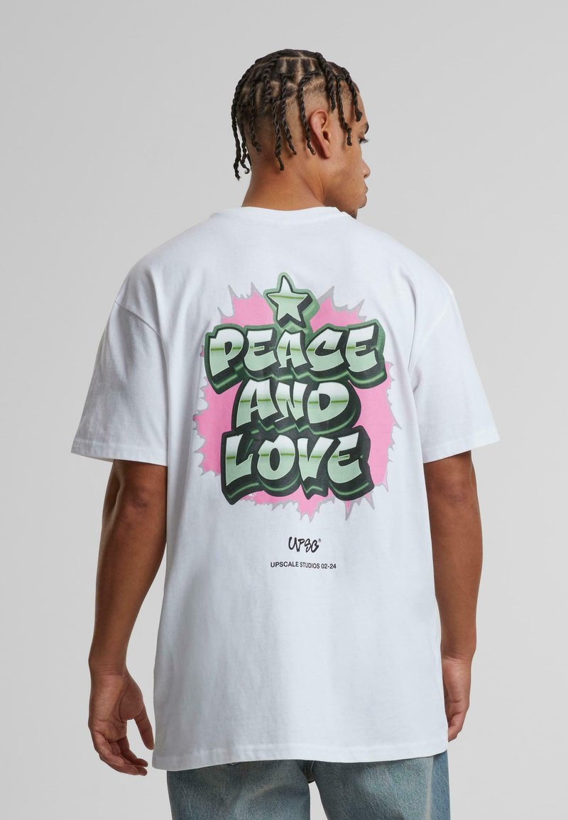 White oversized t-shirt with green and pink graffiti-style "PEACE AND LOVE" text on the back, featuring a star and stylized accents.