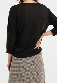 Suéter negro de punto semi-translúcido con mangas de tres cuartos y un corte relajado. Combinado con una falda de patrón de espiga.