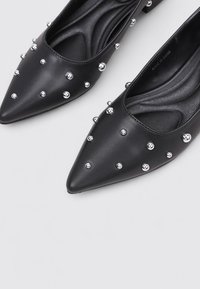 Bailarinas negras de punta afilada, hechas de cuero suave, adornadas con tachuelas plateadas, que cuentan con una plantilla acolchada de diseño texturizado.