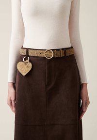 Brown suede skirt with a textured beige belt featuring a gold buckle. A heart-shaped charm hangs from the belt, adding detail to the overall look.