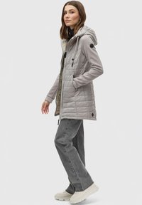 Lys grå quiltet puffer-jakke med hætte, lynlåslukning foran og sidelommer; parret med grå flagrende bukser og hvide sneakers.