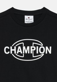 Svart bomull T-skjorte med rund hals og korte ermer. Har en stor hvit "CHAMPION"-logo i midten. Merket med merkeetikett.