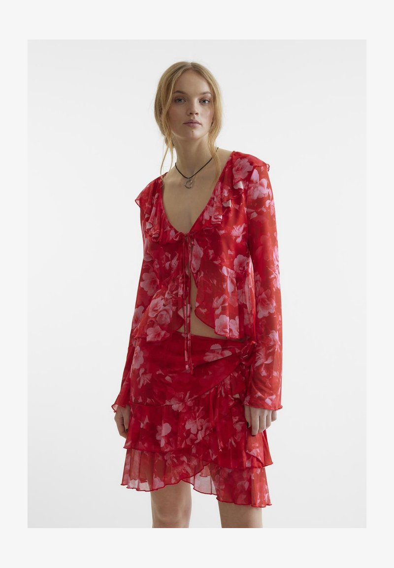 Punane lillemustriga läbipaistev pluus volangidega servades ja sobiv kihiline seelik. Kerge kangas, pikad varrukad ja nööriga detailid.