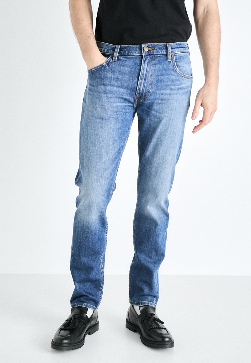 Light blue straight-leg jeans in denim fabric, featuring five pockets, a button closure, and subtle fading for texture. Worn with black shoes.