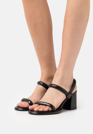 Sandales à talons noirs avec deux larges sangles en cuir et un embout carré. Le talon épais est solide et lisse avec une finition brillante.