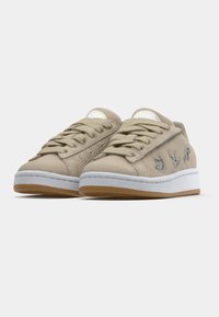 Világos bézs színű, velúr anyagú sportcipő fehér középtalppal és gumitalppal. Fűzős kialakítású, oldalán hímzett részletekkel.