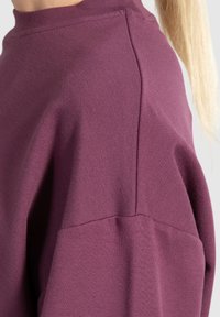 Felpa viola con collo alto, vestibilità oversized e tessuto textured. Il tessuto presenta un sottile motivo a coste e spalle senza cuciture.