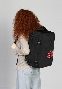 Mochila negra de nailon con un destacado logo de nube roja. Tiene correas ajustables, compartimentos con cremallera y una forma rectangular elegante.