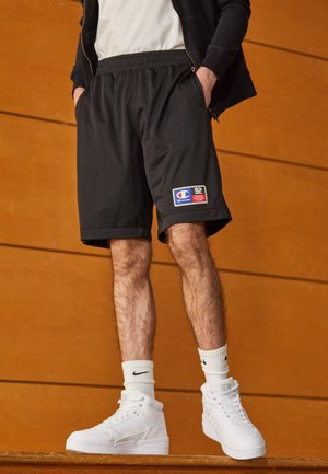 Czarne sportowe szorty z teksturowanej tkaniny, elastycznym pasem i bocznymi kieszeniami, z naszywką z logo Champion. W zestawieniu z białymi trampkami typu high-top.