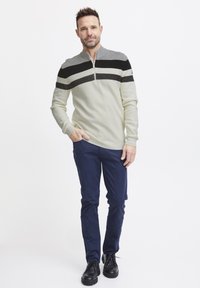 Sweater in light beige with black and dark gray horizontal stripes, quarter-zip collar. Paired with navy trousers and black shoes.