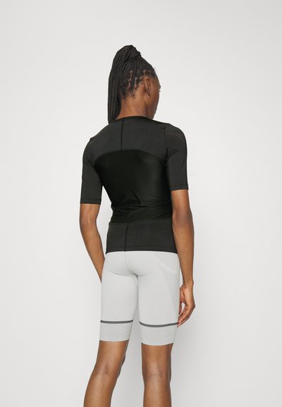 Black fitted athletic top with short sleeves, featuring textured accents. Paired with light grey cycling shorts, marked with black stripes.