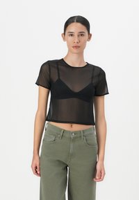 T-shirt cropped in rete nera con maniche corte, caratterizzato da un collo a giro e indossato sopra un bralette nero. Abbina a pantaloni larghi verde oliva.