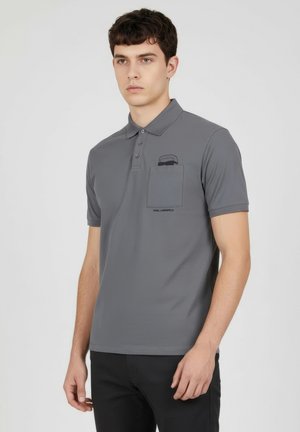 Grå pikétröja med krage, treknappslå, korta ärmar och en bröstficka med en grafisk design. Mjuk textur, figurnära passform.