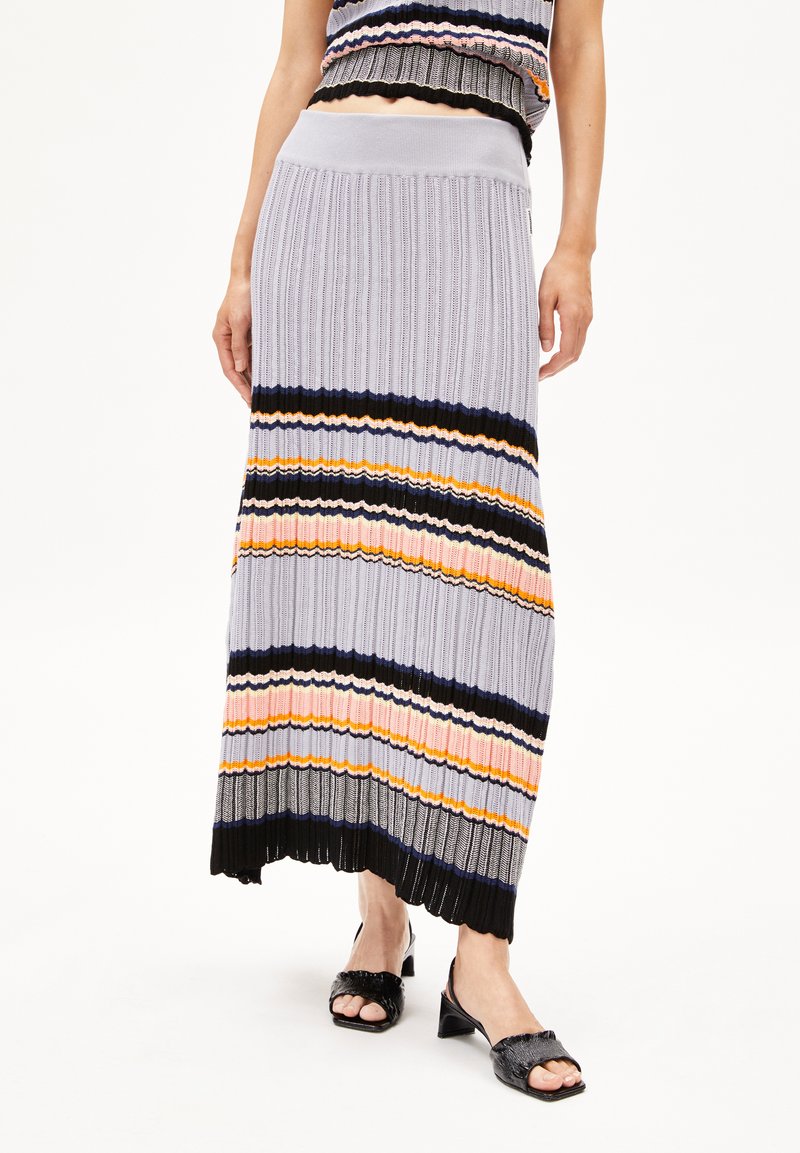 Gebreide maxi-rok in lichtgrijs, met veelkleurige horizontale strepen, geribbelde textuur en geschulpte zoom. Gecombineerd met zwarte hoge sandalen.