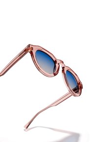 Päikeseprillid läbipaistva roosa raami, ovaalse kujuga, sinise gradientläätse ja õhukeste sangadega, millel on logoga detail.