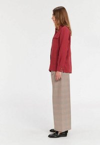 Chemise rouge à boutons avec poche plaquée, associée à un pantalon large à carreaux beige et à des mocassins noirs. Tissu lisse et coupe ajustée.