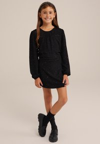 Svart klänning med långa ärmar, texturerad tyg och flerfärgade prickar. I kombination med svarta loafers och knästrumpor. Enkel hårsno.