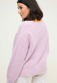 Maglione lavorato a maglia lilla con una vestibilità rilassata, spalle ribassate e orlo a costine. Presenta un colletto giallo a contrasto sul retro.