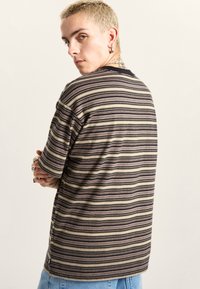 Camiseta a rayas en tonos negro, beige y oliva. Mangas cortas, escote redondo, corte relajado, con detalle en la costura lateral.