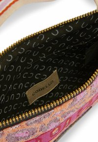 Tasche mit Reißverschluss, Außenseite in pink-orange Muster, goldene Reißverschlussbeschläge und schwarzes Innenfutter mit einem Logo und geschwungenem Textdesign.