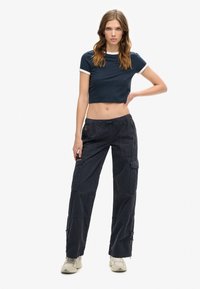 Marine crop top med hvid kant, parret med løstsiddende sorte cargo bukser med lynlåse i lommerne og justerbare manchetter.