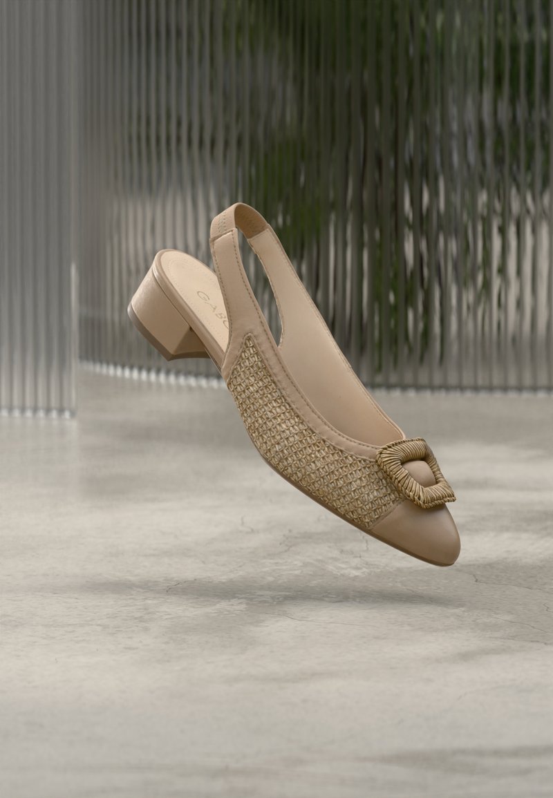 Μπεζ γόβα με λουράκι και χαμηλό τετράγωνο τακούνι. Διαθέτει πλεκτή λεπτομέρεια από άχυρο στο πλάι και τετράγωνο πλεκτό διακοσμητικό στη μύτη.