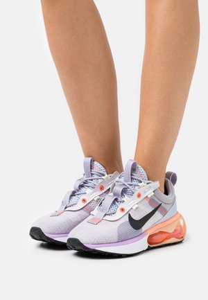 Baskets de sport en mesh et tissu lavande, avec un logo Nike noir, des accents pastel et une semelle amortissante à coussin d’air orange.