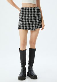 Minifalda de cuadro de ajedrez en blanco y negro con dobladillo desflecado, combinada con botas de cuero negro hasta la rodilla. Textura suave con un diseño estructurado.