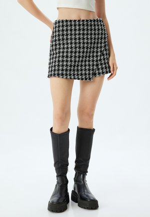 Gonna mini in bianco e nero a motivo houndstooth con orlo sfilacciato, abbinata a stivali neri in pelle alti fino al ginocchio. Tessuto liscio con design strutturato.