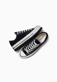 Zapatillas de lona azul marino con costuras blancas, punteras de goma y suelas negras gruesas. Cuenta con un diseño de cordones con ojales visibles y branding en el interior.
