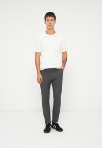 Bílý krátký úvazkový polo s texturovaným pruhovaným vzorem, spárovaný s tmavě šedými slim-fit kalhotami a černými teniskami s bílými akcenty.