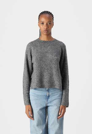 Suéter gris de punto con cuello redondo, mangas largas y corte relajado. Textura suave, estilo ligeramente recortado, combinado con jeans de color azul claro.