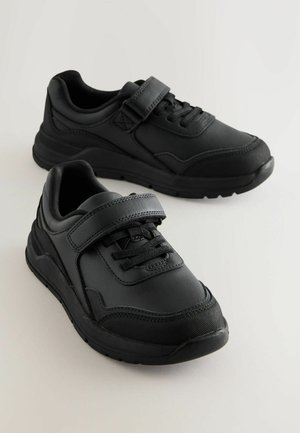 Des chaussures de sport noires avec un dessus en synthétique lisse, un design à lacets avec une sangle Velcro, un col rembourré et une semelle en caoutchouc texturé.