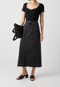 Top corto negro con encaje, combinado con una falda de mezclilla negra de tiro alto con un dobladillo de flecos y tacones bloque abiertos negros.